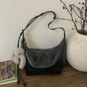 Detail of black wax leather hobo bag with a plush bunny charm on a vintage wooden table