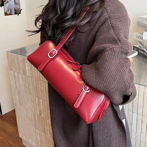 Close-up of dark red cylindrical underarm bag with silver buckles on shoulder straps
