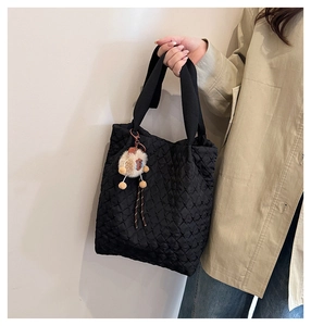 Close-up of black quilted tote bag texture with cute plush doll keychain accessory