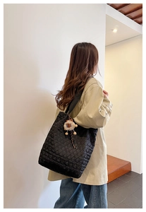 Detail of black quilted tote bag with soft diamond texture and plush animal charm on strap