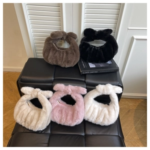 Group of plush handbags in five colors displayed on a black leather bench with natural light