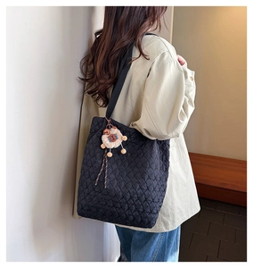 Detail of black quilted tote bag with diamond pattern and cute plush charm pendant