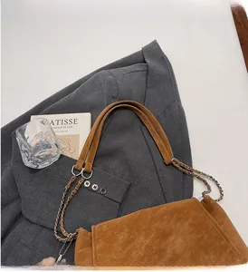 Detail einer braunen Wildleder-Umschlagtasche mit Lederkettenriemen auf weißem Grund