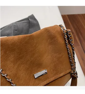 Detailansicht der braunen Wildledertasche mit silbernem Metalllogo und Kettenriemen