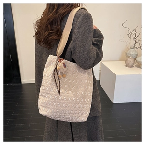 Beige quilted tote bag with diamond pattern and plush charm on a model's shoulder