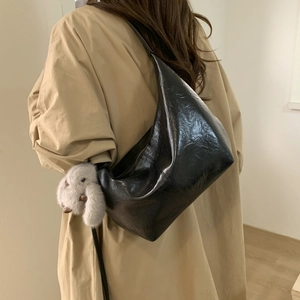 Detail of a black glossy hobo bag featuring a white plush rabbit pendant on the shoulder strap