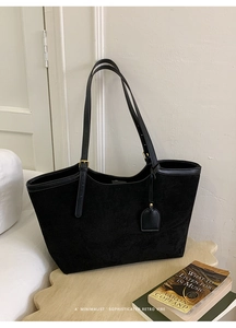Detailed close-up of a black suede tote bag with gold metal buckles and leather trim