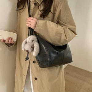 Black hobo shoulder bag with a plush white rabbit charm on a minimalist beige trench coat