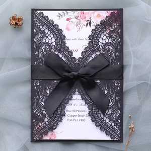 Detail of laser cut lace wedding invitation with black silk bow and floral insert