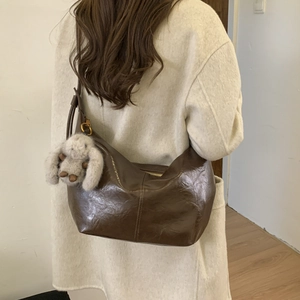 Detail of dark brown wax leather hobo bag with vintage texture and plush rabbit charm
