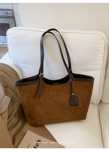 Detail view of brown suede tote bag with leather straps and a retro vibe on a white sofa