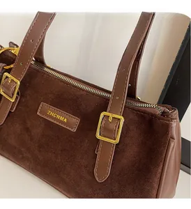 Detail of brown matte leather shoulder bag featuring polished gold buckles and zippers