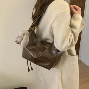 Deep brown glossy Hobo shoulder bag with plush bunny charm on beige wool coat