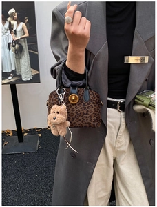Retro leopard print bowling bag with plush puppy charm shown on a stylish grey coat
