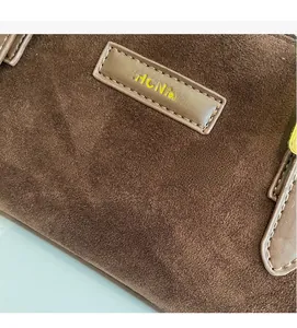 Detail of dark brown faux suede material and embossed logo on minimalist shoulder bag