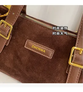 Detail of a brown suede baguette bag featuring golden hardware and leather logo patch