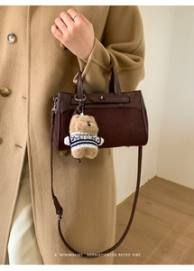 Dettaglio borsa Kelly in pelle marrone scuro con ciondolo orsetto su cappotto