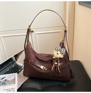Detail of dark brown suede hobo bag with teddy bear charm and gold buckle on a desk