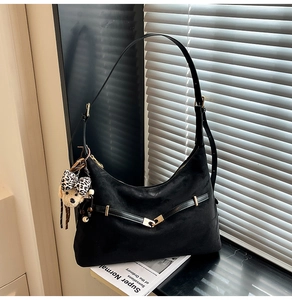 Close-up of black suede dumpling bag with golden buckle and plush dog charm accessory