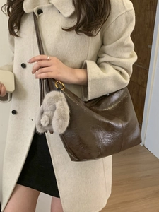 Brown glossy hobo shoulder bag with plush rabbit charm shown on a female model