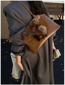 Dettaglio della borsa tote in pelle cerata caramello con ciondolo a cuore e cucciolo di peluche