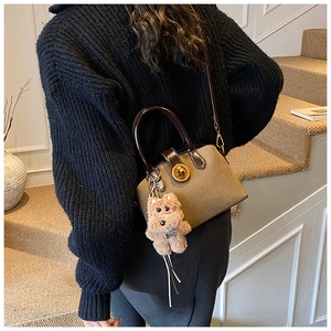 Detail of khaki suede trapezoid handbag with brown handles and plush dog charm