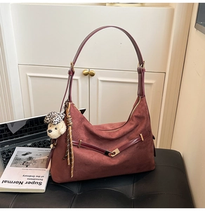 Detail shot of burgundy suede tote bag with gold V-buckle and leopard bear charm