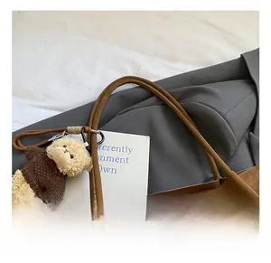 Détail d'un sac cabas en daim marron avec pendentif ours en peluche sur fond de costume gris
