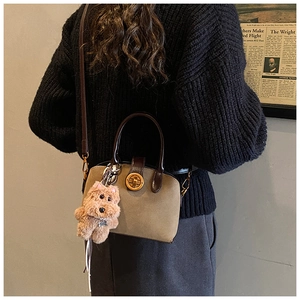 Detail of a retro khaki shell bag with brown leather handles and a plush dog charm