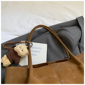 Détail d'un sac cabas en daim marron avec une breloque d'ours en peluche sur l'anse