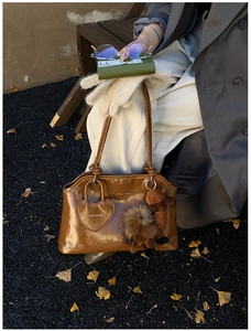 Dettaglio borsa a tracolla in pelle marrone lucida con ciondolo a cammello in peluche
