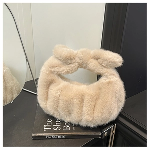 Dettaglio della borsa in ecopelliccia beige con manico a fiocco appoggiata su un libro