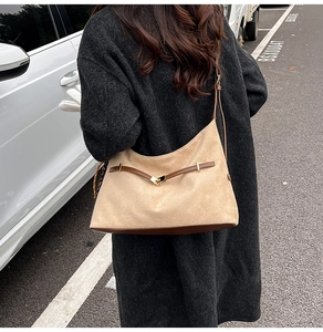 Detail of khaki dumpling bag with brown leather strap and gold buckle on black wool coat