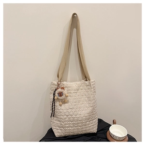 Quilted beige tote bag detail featuring brown teddy bear charm and khaki fabric shoulder strap