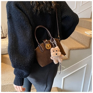 Detail of dark brown suede shell bag featuring a plush puppy charm on a knited sweater