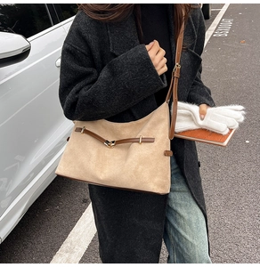 Detail of beige suede dumpling bag with brown leather trim and metal buckle closure