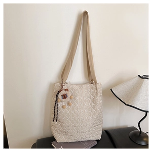 Detail of quilted nylon tote bag with plush bear charm and woven strap in home setting