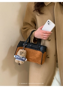 Dettaglio borsa bicolore in pelle con charm a cucciolo su sfondo cappotto invernale beige