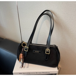 Dettaglio borsa a spalla in camoscio nero con logo dorato e ciondolo con perline decorativo