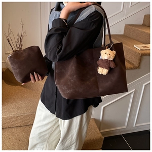 Deep brown suede tote bag with plush bear charm and matching pouch shown on a model