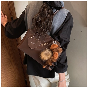 Détail du sac bandoulière marron brillant avec poche cœur et pendentif en peluche chameau
