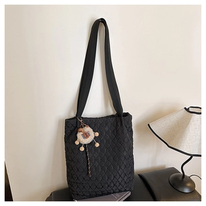 Close-up of black quilted tote bag with a cute plush dog pendant hanging on a white wall