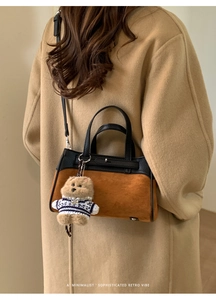 Dettaglio della borsa in pelle bicolore con ciondolo a orsetto su sfondo di cappotto camel
