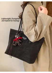 Detail of dark grey suede tote bag featuring a cute brown bear charm with a red bow tie