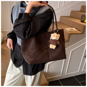 Detail of coffee brown suede tote bag featuring a cute teddy bear charm on the strap