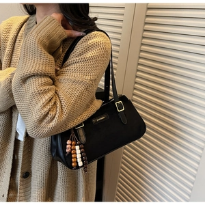 Detail of black leather underarm bag featuring golden hardware and decorative wooden beads
