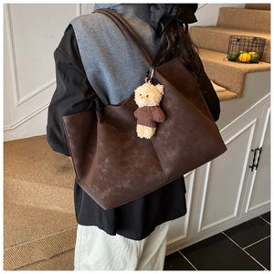 Brown suede tote bag with a small plush bear pendant shown on a model on stairs