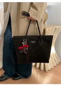 Deep brown oversized tote bag with plush bear charm worn by a model in a beige coat