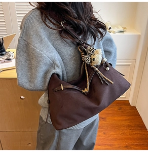 Detail of dark brown suede shoulder bag with bear charm and woven tassel accents