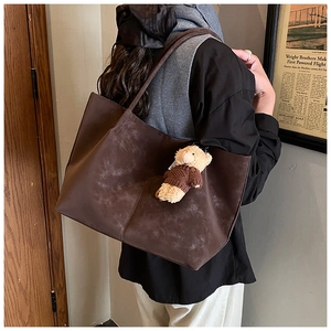 Detail view of large brown suede tote bag with teddy bear pendant on shoulder